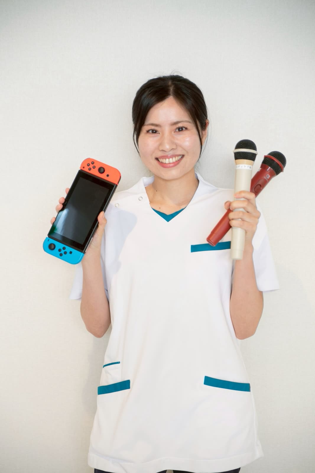 ゲーム機とカラオケマイクを手にしたレクリエーション担当の制服姿のスタッフ